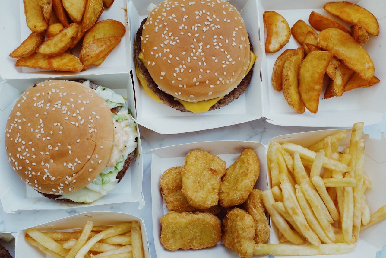 Top view of yummy junk food consisting of burgers and french fries with nuggets placed in boxes on marble background