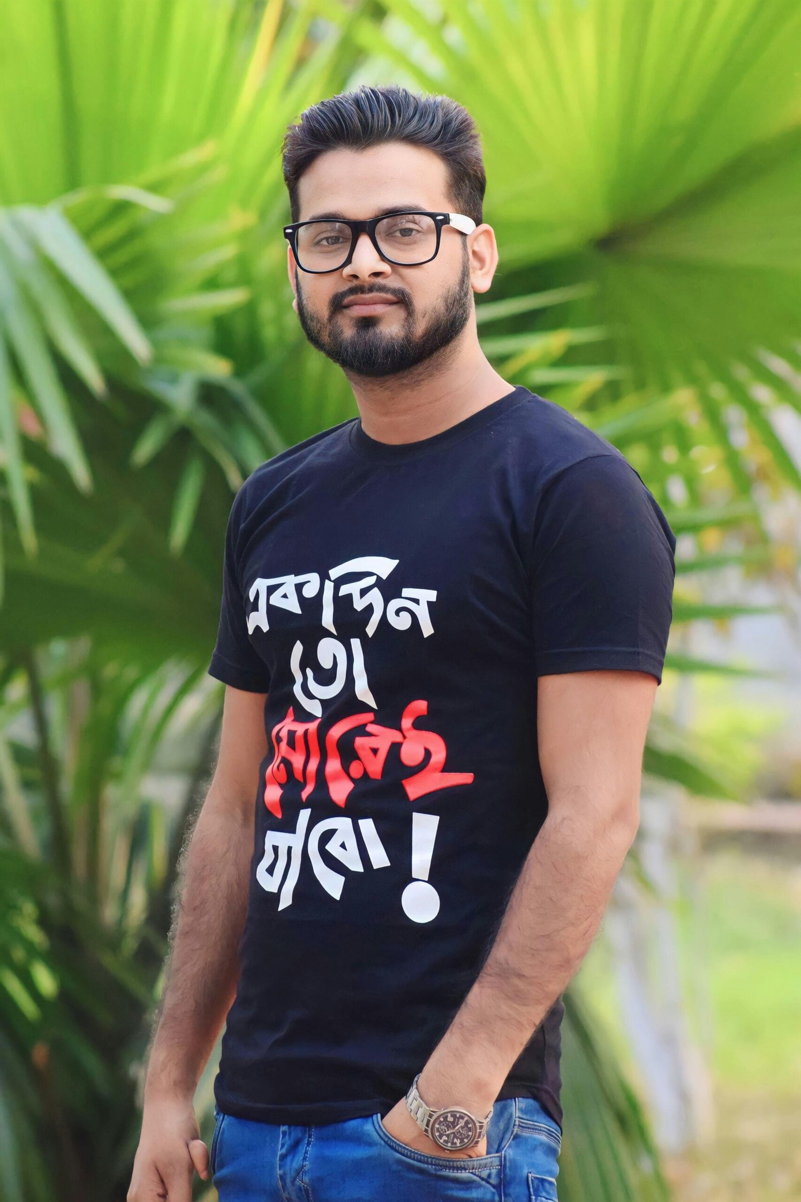 Portrait of a man wearing glasses and a printed T-shirt surrounded by tropical plants.